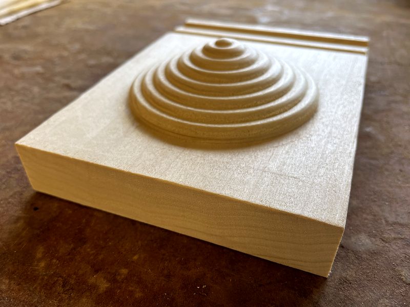Maple plinth block with a carved bull's-eye rosette, 45-degree view